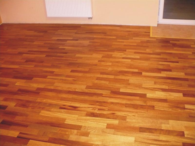 Ułożony parkiet z drewna w odcieniach brązu, widoczny grzejnik i fragment okna w tle.